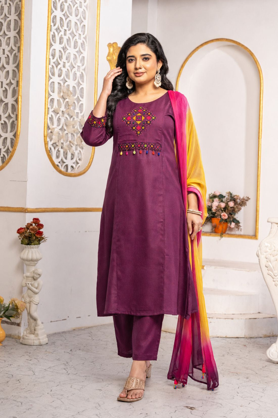 Model wearing a magenta pure cotton kurta pant set featuring multicolour geometric cross-stitch embroidery with mirror detailing, three-quarter sleeves, straight-fit pants and an ombre tie-dye chiffon dupatta.