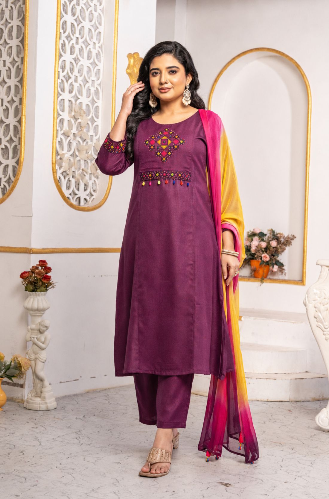 Model wearing a magenta pure cotton kurta pant set featuring multicolour geometric cross-stitch embroidery with mirror detailing, three-quarter sleeves, straight-fit pants and an ombre tie-dye chiffon dupatta.