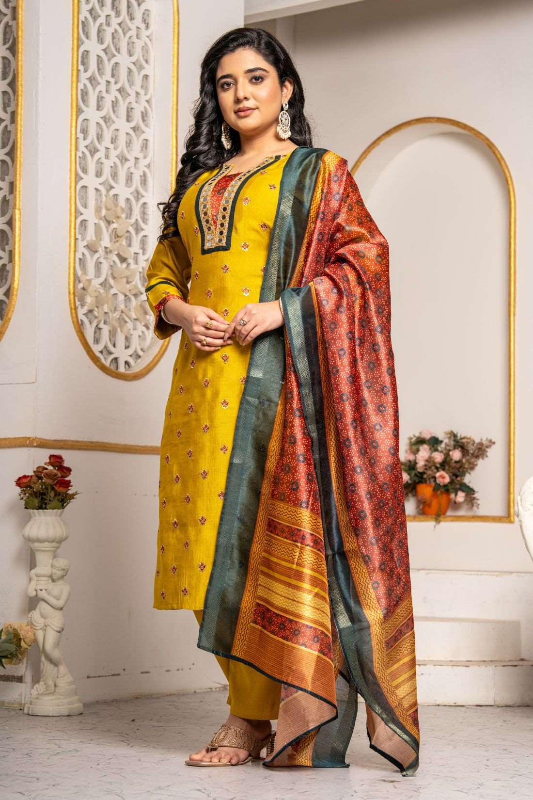 Model wearing a mustard yellow Vichitra silk kurta set featuring a mirror-work V-neckline, contrast Bandhani-print panel, sequin and thread embroidery, straight pants, and a printed Chanderi silk dupatta.