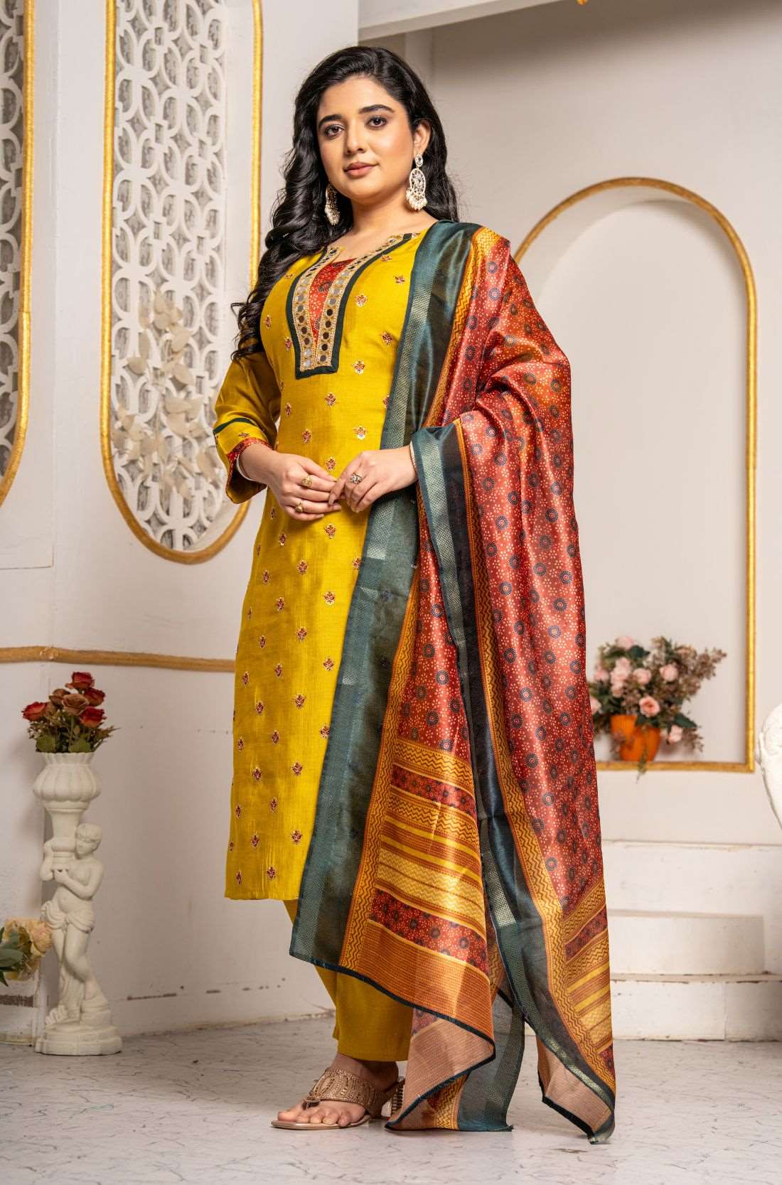 Model wearing a mustard yellow Vichitra silk kurta set featuring a mirror-work V-neckline, contrast Bandhani-print panel, sequin and thread embroidery, straight pants, and a printed Chanderi silk dupatta.