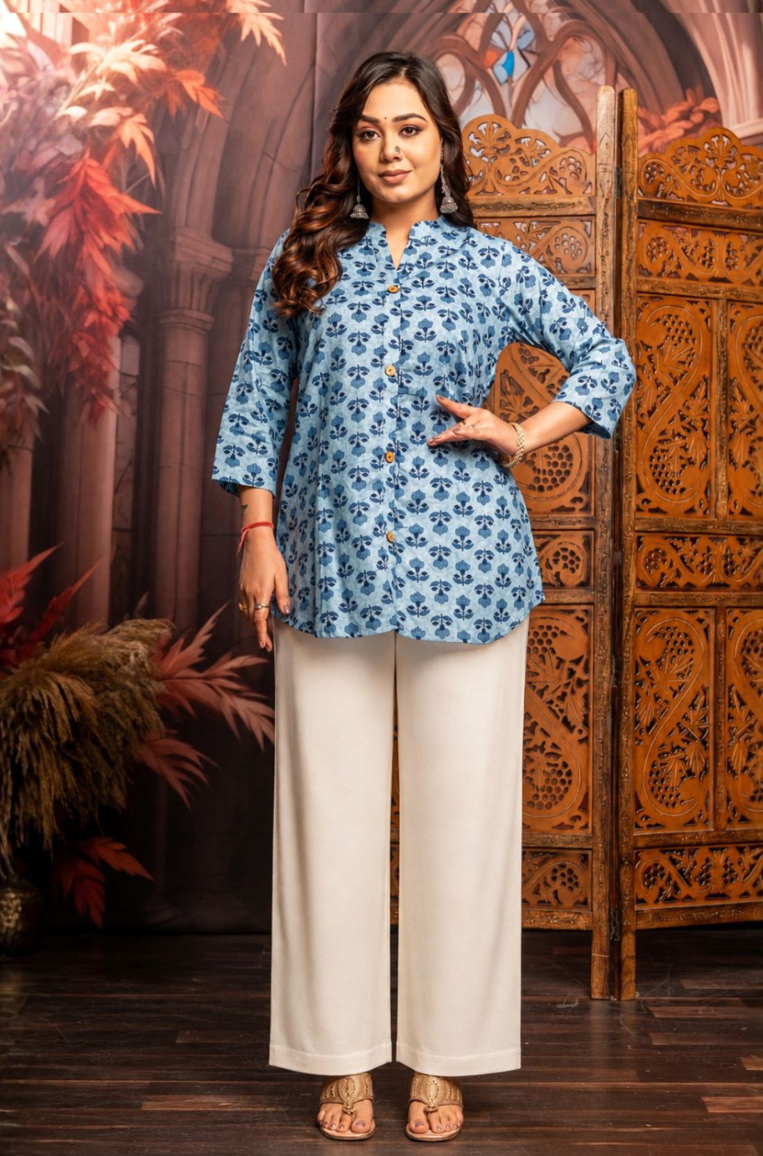 Front view of women's powder blue short kurti crafted from pure cotton with hand block floral print, wooden button placket, 3/4 sleeves, mandarin notch neckline, relaxed fit and side slits paired with white palazzo pants.