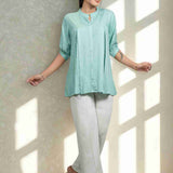Front view of women's sea green rayon Top featuring a mandarin collar, button-down front, front pleats, half sleeves, and a relaxed fit paired with white trousers.