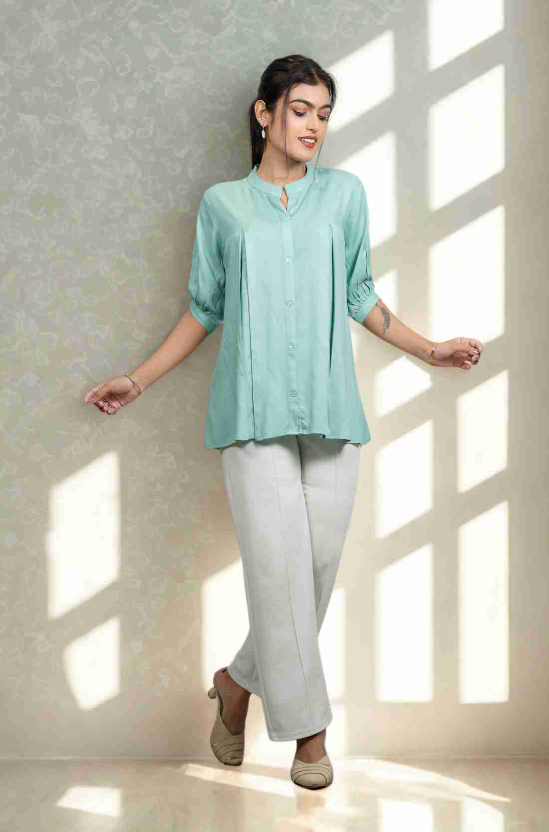 Front view of women's sea green rayon Top featuring a mandarin collar, button-down front, front pleats, half sleeves, and a relaxed fit paired with white trousers.