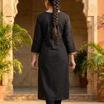 A woman seen from the back, showcasing the simple black straight kurta and her braided hairstyle.