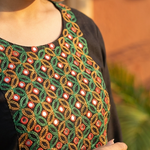 A close-up view of the neckline of a black kurta, highlighting detailed green, red, and gold mirror-work embroidery.