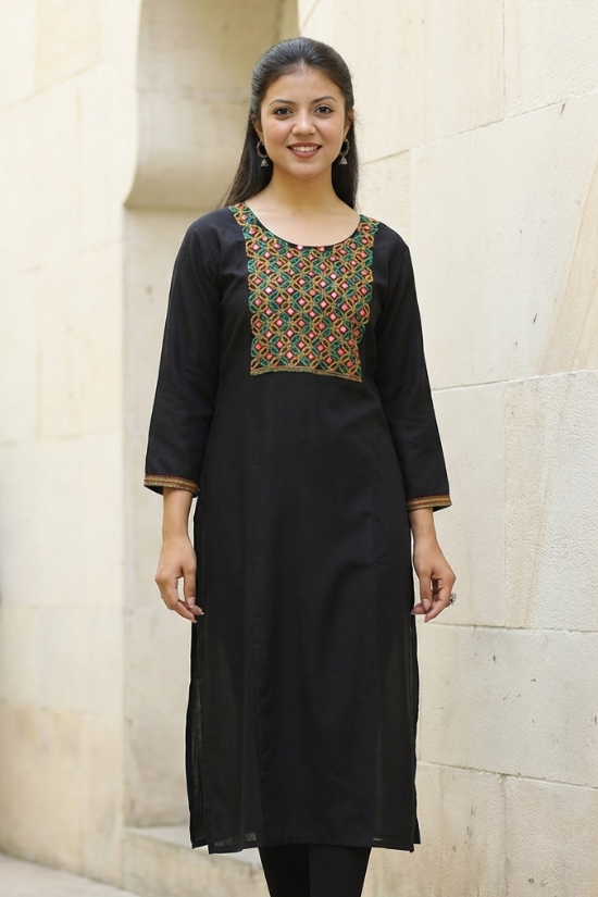 A front-facing studio shot of a woman modeling a black straight-cut kurta with mirror-work detailing.