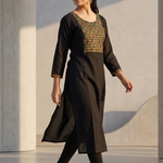 A woman walking in a black kurta paired with black leggings, showcasing the outfit's silhouette.