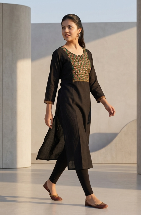 A woman walking in a black kurta paired with black leggings, showcasing the outfit's silhouette.