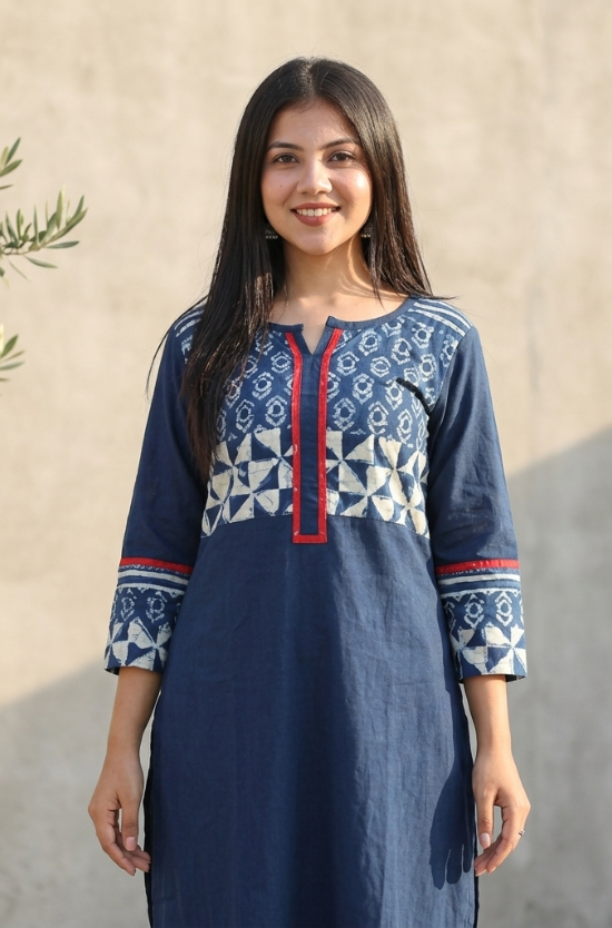 Smiling woman wearing a dark blue kurti featuring a geometric and floral printed yoke with red piping.