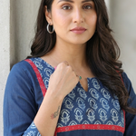 Close-up portrait of a confident woman wearing a blue kurti with red paneling and subtle floral prints.