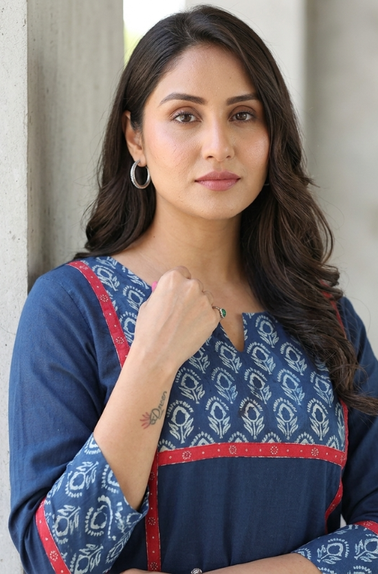 Close-up portrait of a confident woman wearing a blue kurti with red paneling and subtle floral prints.