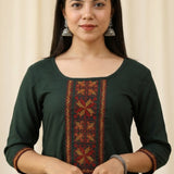 Close up shot of a bottle green rayon ethnic kurti for women featuring elegant red and gold geometric embroidery panel on the front bodice and matching trim borders on the three quarter sleeves.