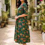 Side profile view of a woman posing in a flared dark green cotton floral print frock-style kurti, highlighting the comfortable elbow-length sleeves and elegant drape.