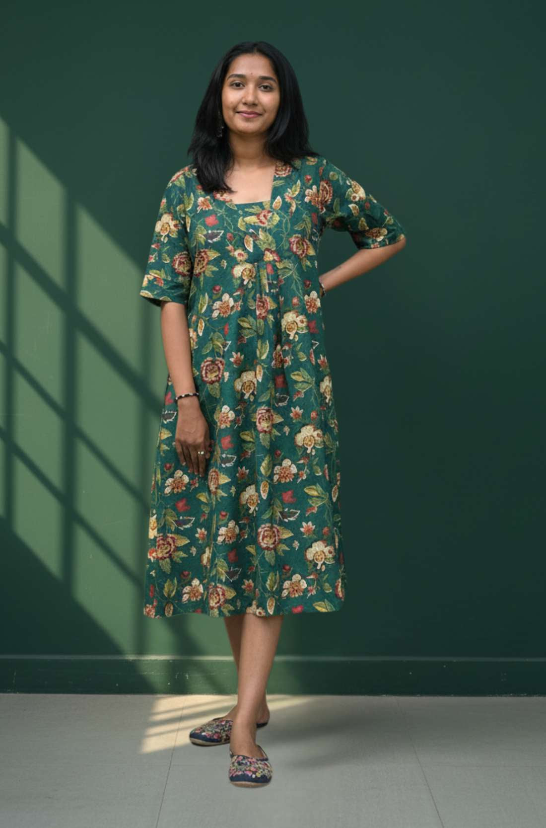 Woman wearing a dark green floral cotton midi dress with v neckline and short sleeves, front view.