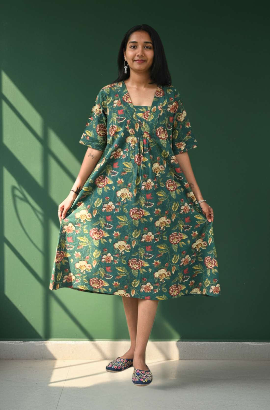 Model holding the flared dark green floral midi dress showing flowy A-line fit from the front.