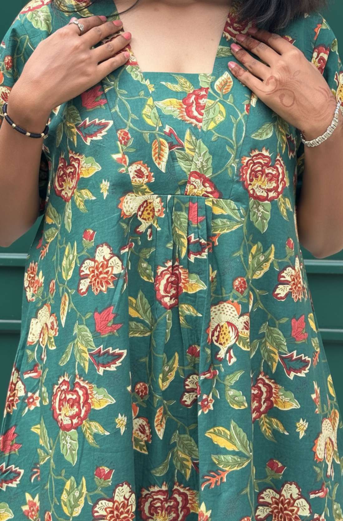 Close-up of V neckline and pleated front on dark green floral cotton midi dress.