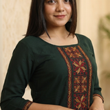 A woman wearing a dark green kurta with intricate gold and maroon ethnic embroidery on the neckline.