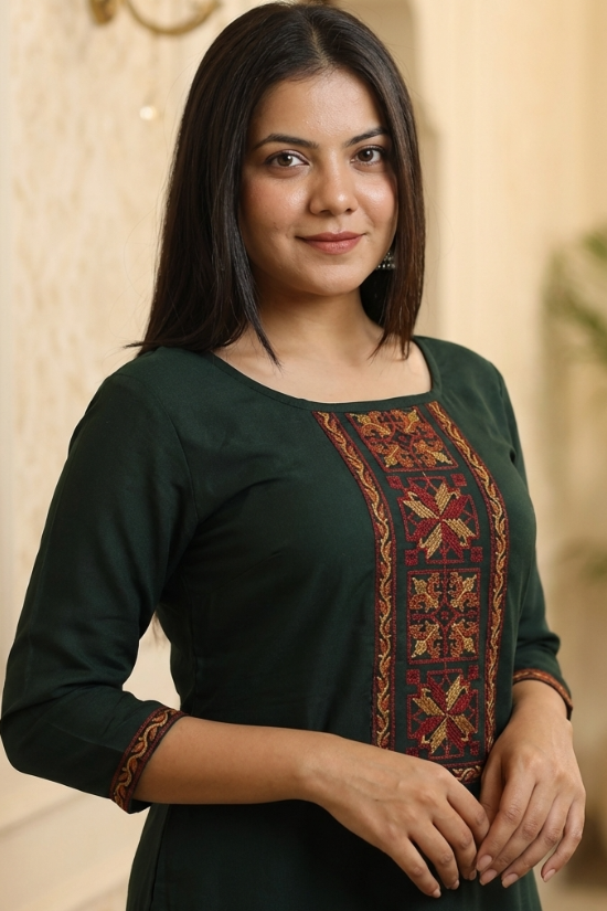 A woman wearing a dark green kurta with intricate gold and maroon ethnic embroidery on the neckline.