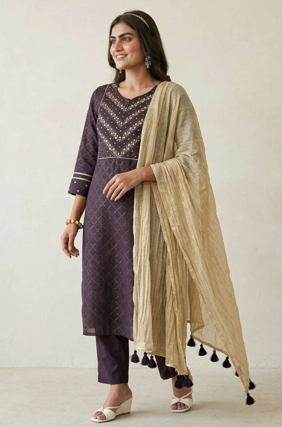Left side angled view of a woman posing in a premium dark purple pure crepe hand embroidered kurta set displaying the complete festive outfit