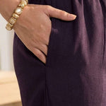 Close up utility view highlighting the convenient functional side pocket tailored seamlessly into the matching straight trousers of a dark purple crepe hand embroidered suit set, with a hand resting inside.