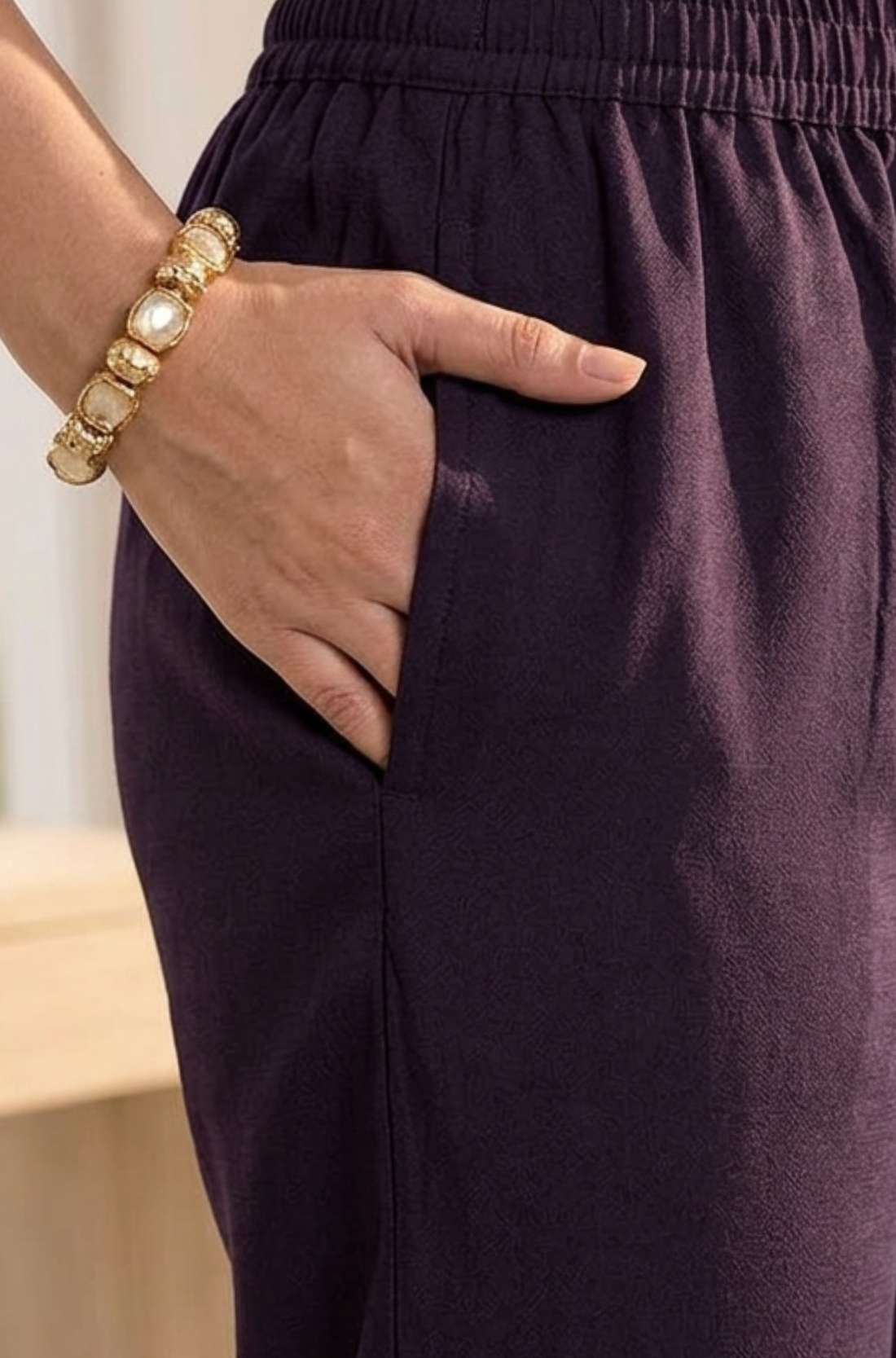 Close up utility view highlighting the convenient functional side pocket tailored seamlessly into the matching straight trousers of a dark purple crepe hand embroidered suit set, with a hand resting inside.