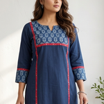 Woman standing indoors wearing an elegant blue office wear kurti featuring a printed neckline and red accents.