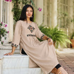 Model sitting in embroidered beige A-line rayon kurta with cross stitch yoke and sleeve detail