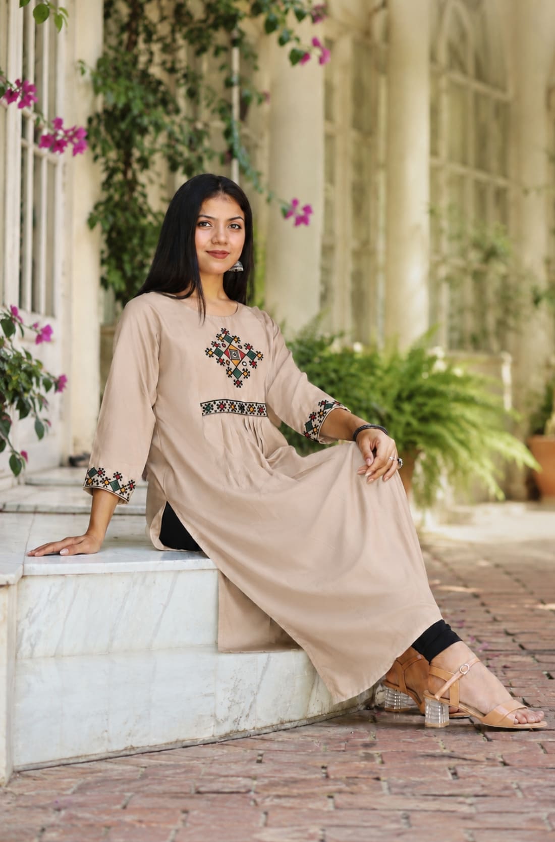 Model sitting in embroidered beige A-line rayon kurta with cross stitch yoke and sleeve detail