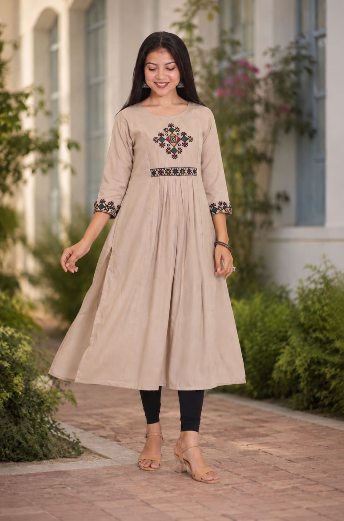 Model wearing embroidered beige A-line rayon kurta with flared hem and black leggings, walking front view
