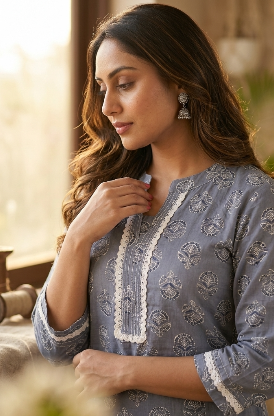 A woman standing sideways, modeling a grey-blue straight-cut kurta with white lace trim and white trousers.