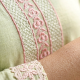 Close-up shot of light green fabric showing detailed pink floral embroidery on the neckline and sleeve cuffs.