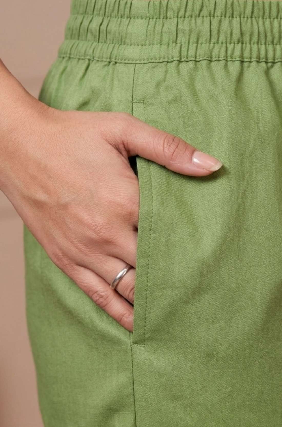 Close up view showcasing a functional side utility pocket tailored into a light green pure cotton kurta with vibrant floral cross stitch embroidery details, with a hand resting inside the pocket over straight pants.