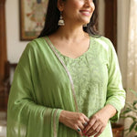 Close up shot of the delicate white thread embroidery, lace trims, and pintucks detailing on the neckline of a light green cotton kurta