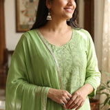 Close up shot of the delicate white thread embroidery, lace trims, and pintucks detailing on the neckline of a light green cotton kurta