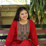 A model sitting on a bench while wearing a maroon rayon round-neck A-line kurta with 3/4 sleeves and a block-printed embroidered yoke