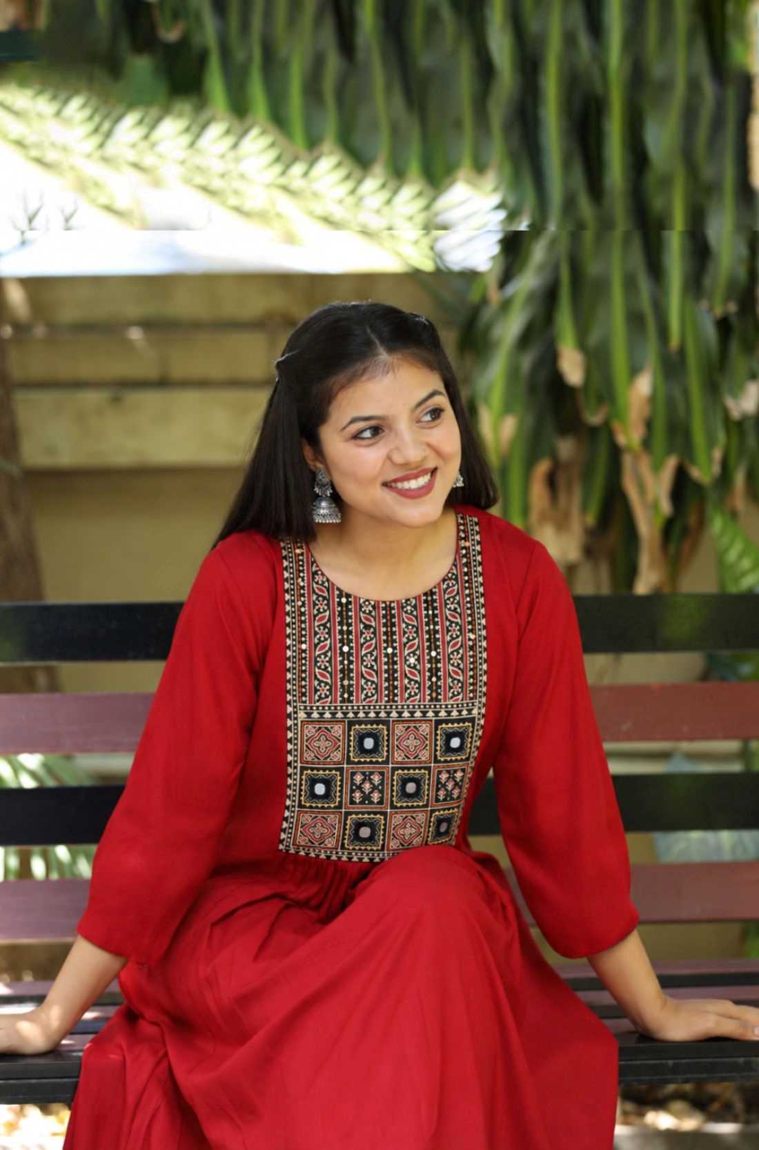 A model sitting on a bench while wearing a maroon rayon round-neck A-line kurta with 3/4 sleeves and a block-printed embroidered yoke