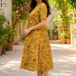Side profile view of a woman wearing an mustard yellow cotton floral print frock-style kurti dress, showcasing the relaxed-fit elbow sleeves and A-line drape.