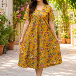 Full-length view of a woman showcasing a bright mustard yellow pure cotton frock-style kurti with an all-over traditional floral print in red and green hues.