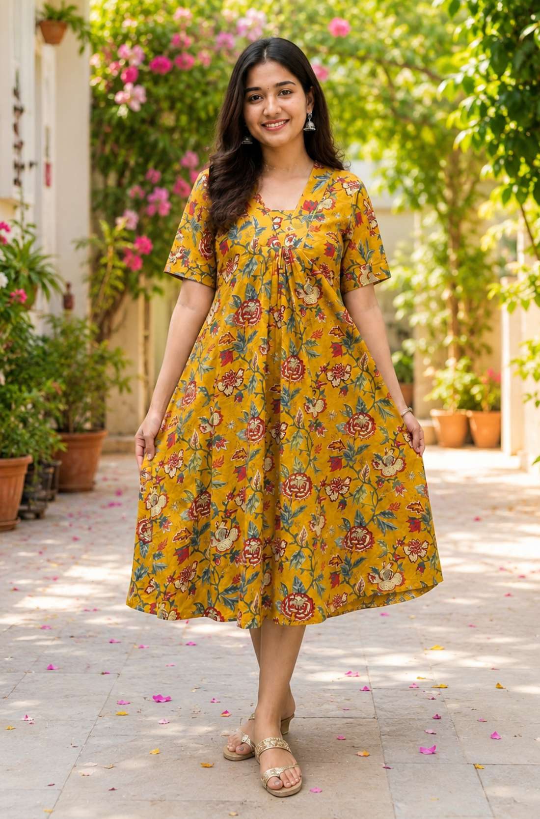 Full-length view of a woman showcasing a bright mustard yellow pure cotton frock-style kurti with an all-over traditional floral print in red and green hues.