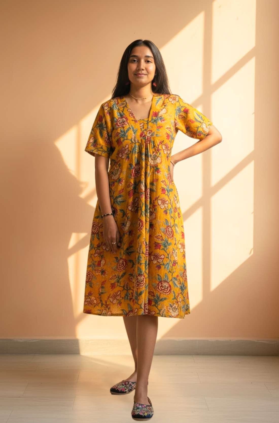 Woman wearing a mustard yellow floral cotton midi dress with short sleeves and gathered front, full front view.