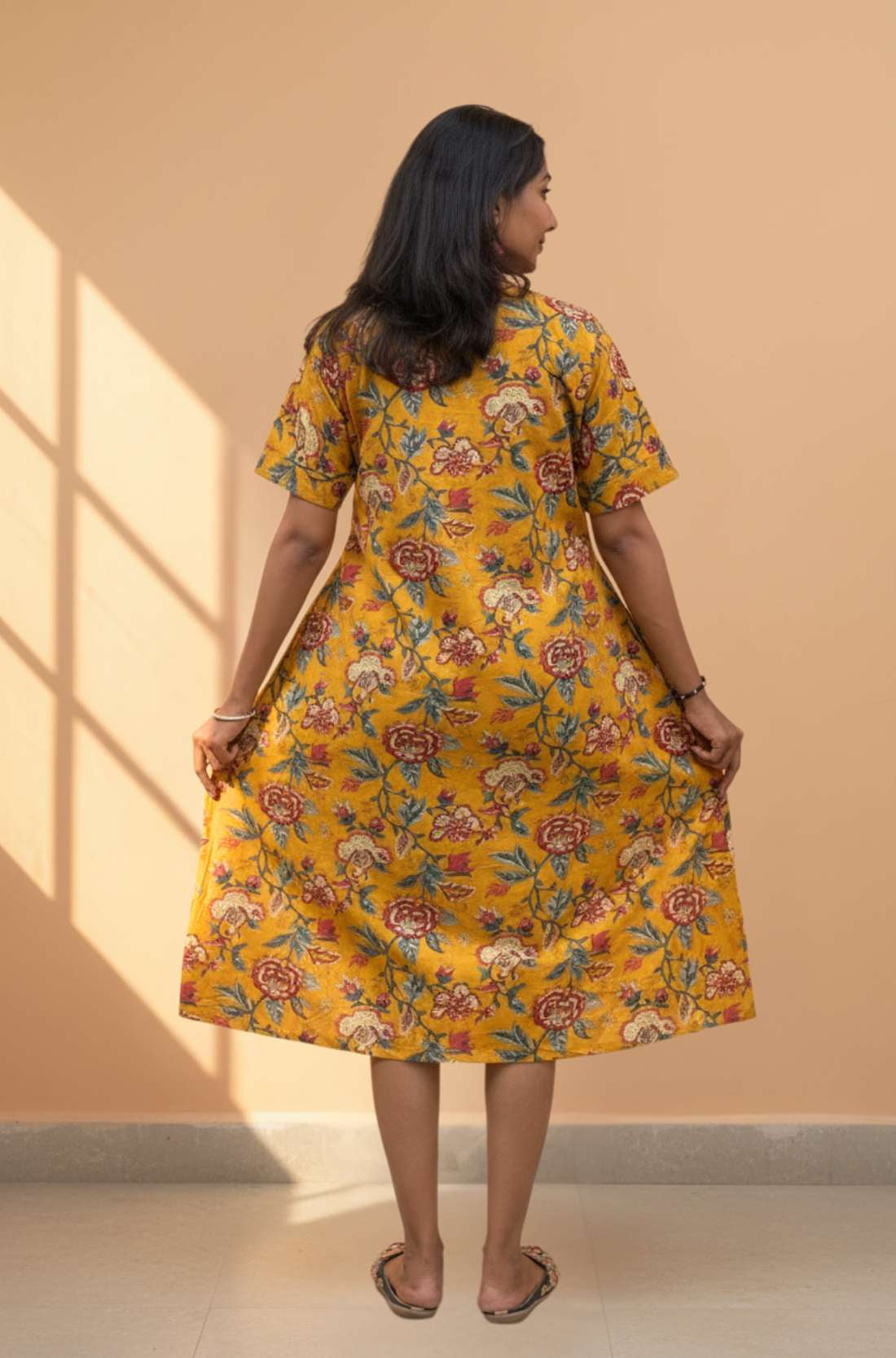 Back view of mustard yellow floral cotton midi dress with short sleeves and relaxed silhouette.