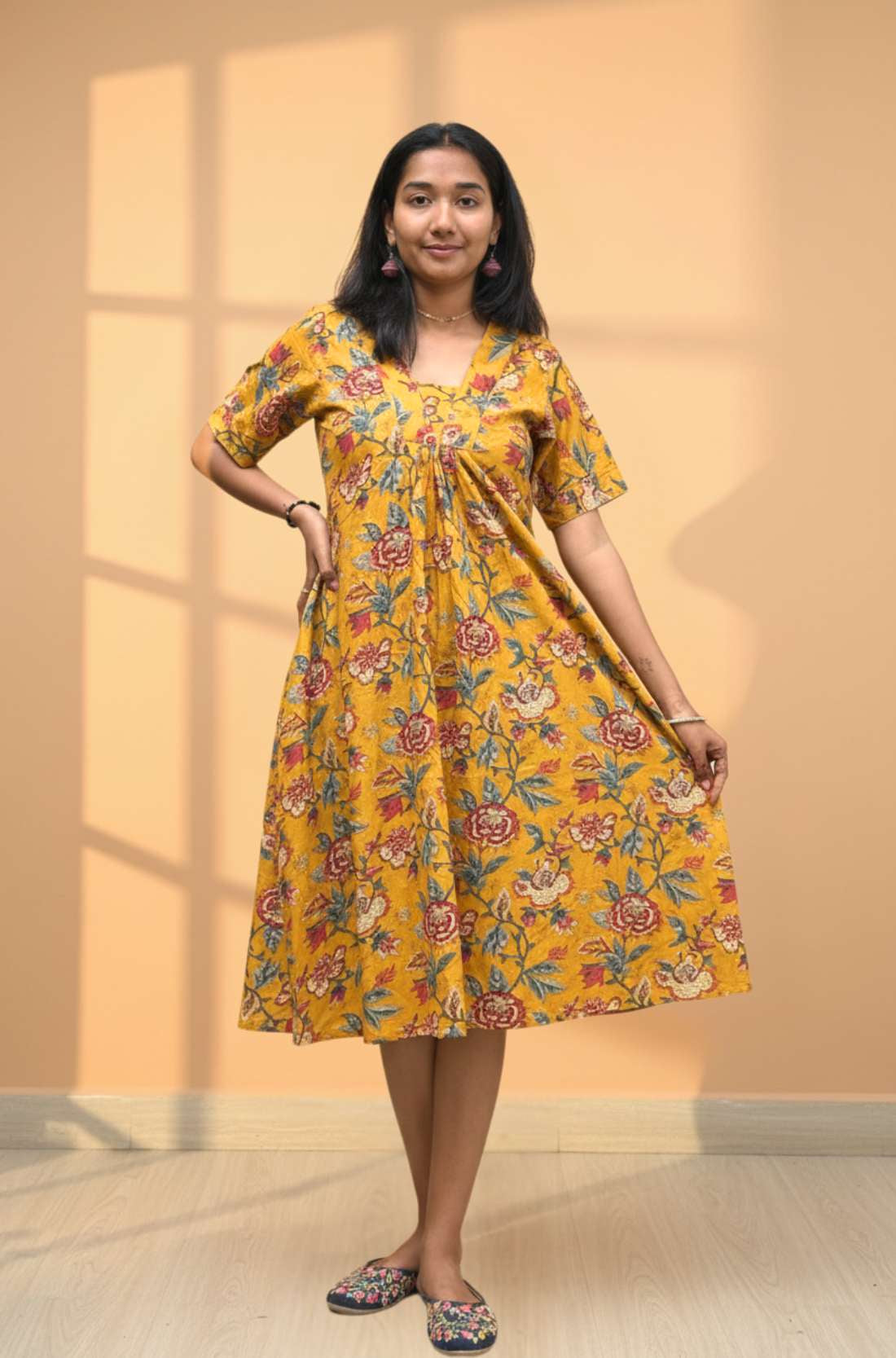 Model holding the flared mustard yellow floral midi dress showing A-line flowy fit from the front.