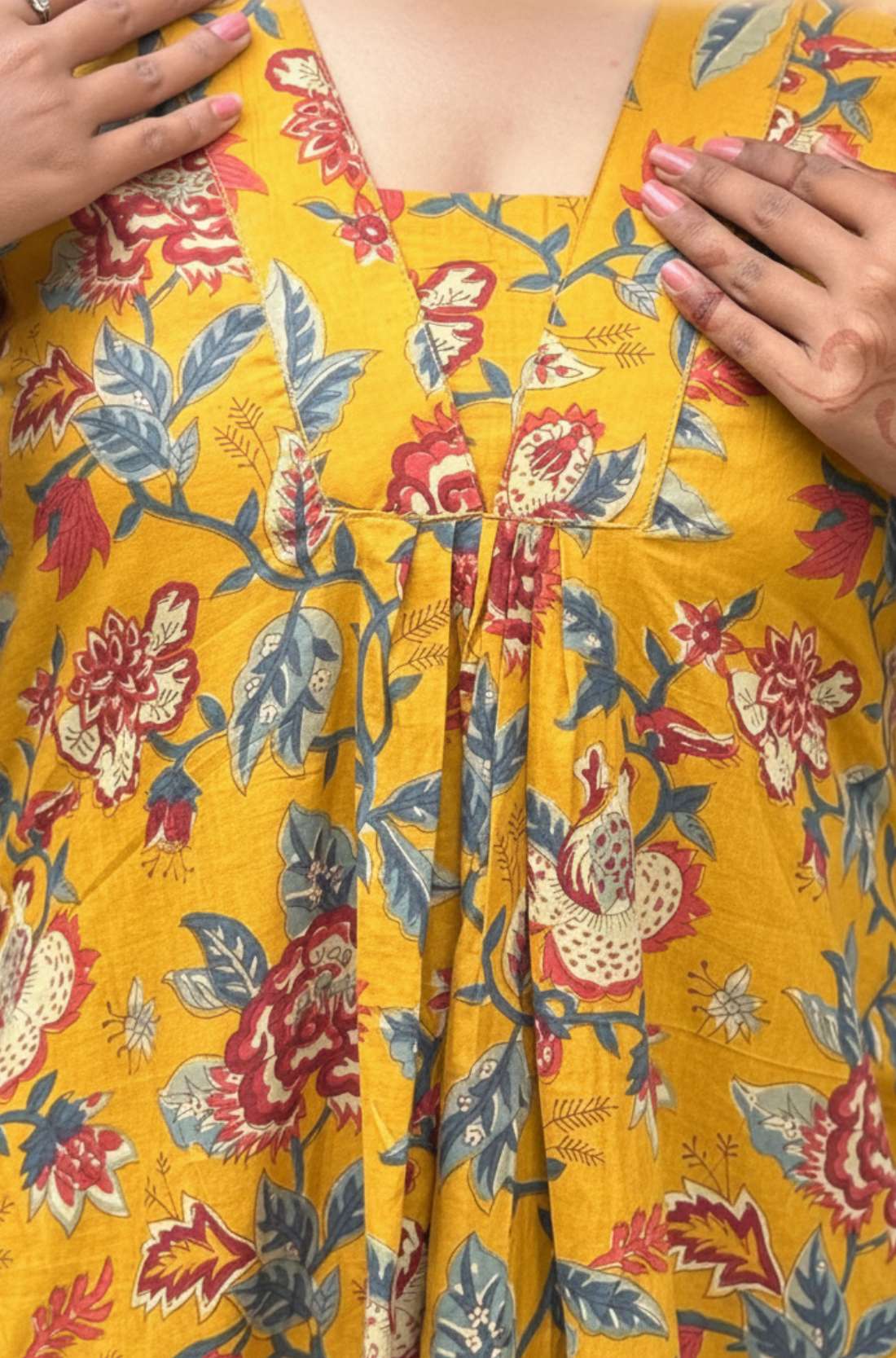 Close-up of V neckline and pleated front on mustard yellow floral cotton midi dress.