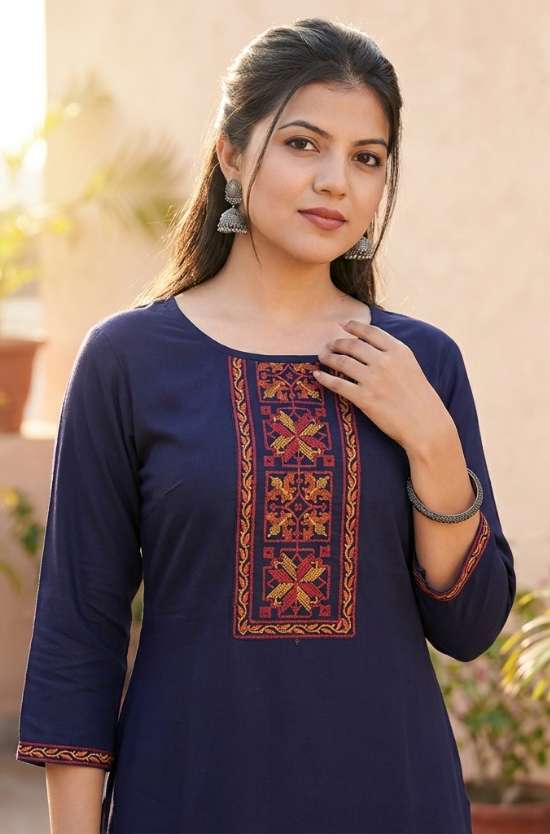 Close-up portrait of a woman wearing a navy blue straight kurta with intricate red and orange ethnic embroidery on the neckline.