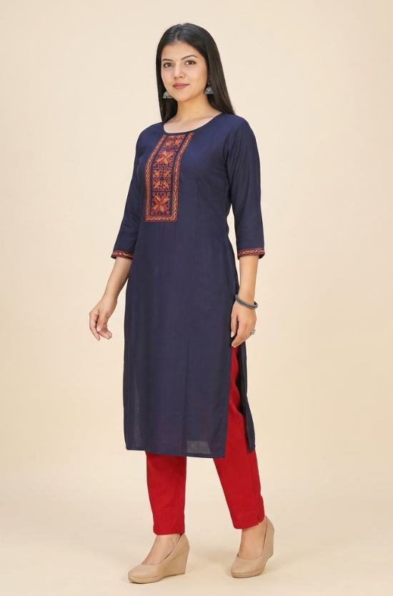 A woman standing in a navy blue straight kurta paired with red trousers, showcasing a professional ethnic look.