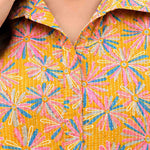 Close-up of ochre yellow cotton midi dress showing the shirt collar, V-shaped opening, front placket and pink blue floral print.