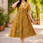 A woman posing gracefully in an ochre yellow pure cotton floral printed frock-style kurti dress, capturing the flowy movement of the flared hemline.