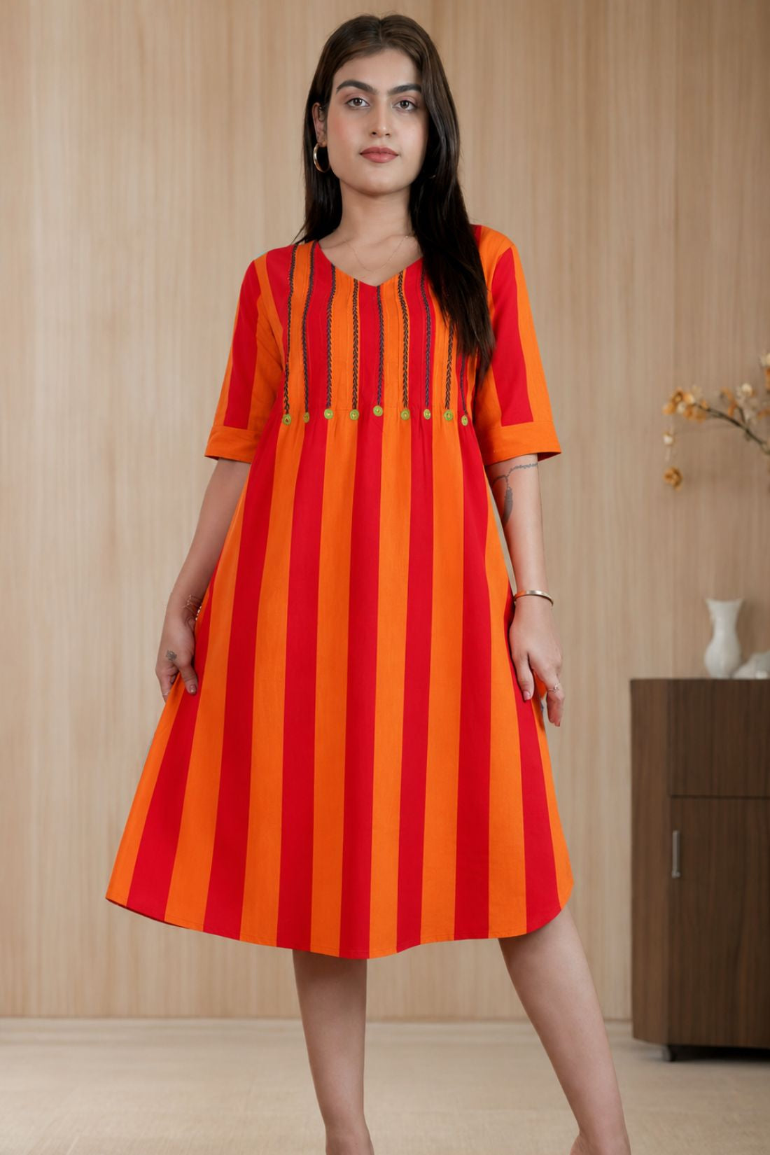Model posing in a pure handloom cotton pintucks tunic in vibrant orange and red vertical stripes with embroidered V-neck detailing and elbow-length sleeves.