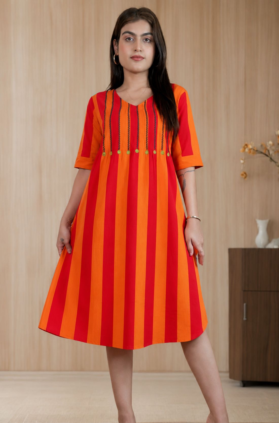 Model posing in a pure handloom cotton pintucks tunic in vibrant orange and red vertical stripes with embroidered V-neck detailing and elbow-length sleeves.