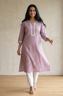 A woman standing in a purple printed ethnic kurta paired with white trousers, displaying a casual yet stylish look.